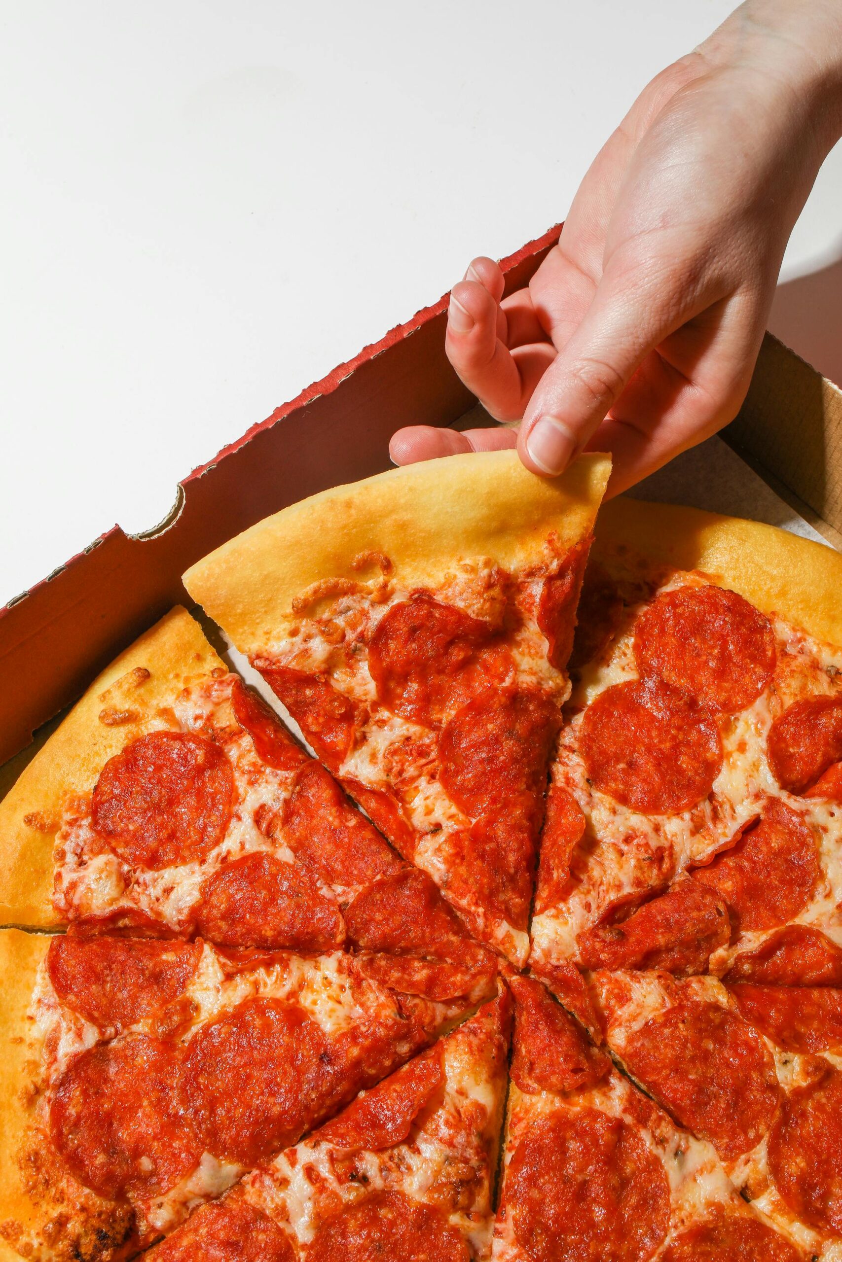 Close-up of a hand picking a pepperoni pizza slice from a box.